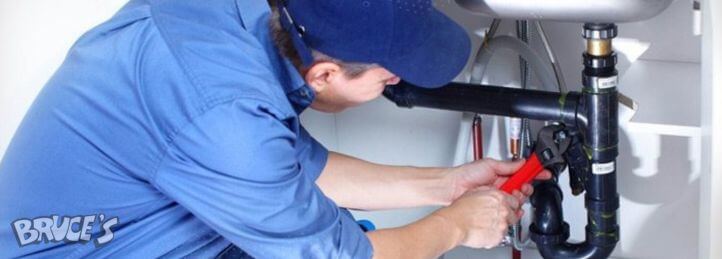 Plumber tightening sink drain pipes with red pipe wrench during under-sink plumbing repair.
